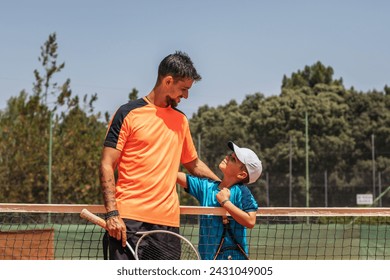 A man and a boy after a tennis match on a dirt court. They are father and son and the father trains him. Two generations sharing a passion for a sport. - Powered by Shutterstock