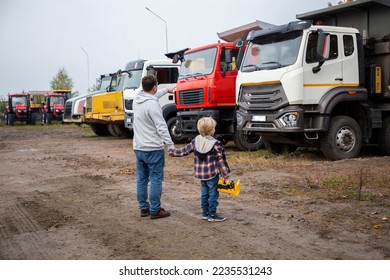 man and a boy, father and son, stand with their backs in front of large trucks. The child's passion for cars, dad and child look at the cars in the parking lot with interest - Powered by Shutterstock