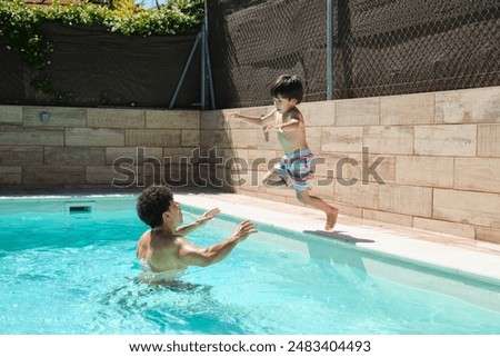 A man and a boy are playing in a pool. The boy is jumping into the water