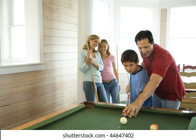 Man And Boy Shooting Pool With Woman And Girl In Background. Horizontally Framed Shot.