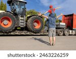 man and boy sitting on his shoulders stand in front of large tractor loaded on truck trailer. son