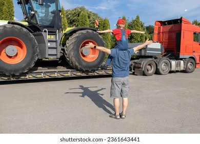 man and boy stand in front of large tractor standing on truck trailer, rear view. son's passion for cars, dad and child look at vehicles in the parking lot with interest. Father's Day, be together - Shutterstock ID 2361643441