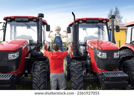 man and boy stand in front of large red new tractors at sales site. An adult and child look at agricultural machinery with interest and show its power. Father's Day, spend time together, be like dad.