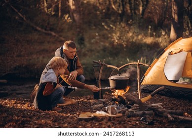 Man and boy tourists autumn time leisure, vacation hiking or traveling touristic activity. Family camping, father and little son relax in forest camp at fire. - Powered by Shutterstock