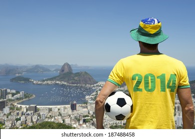 Man in Brazil hat and 2014 shirt standing with football bright sunny Rio de Janeiro skyline with Sugarloaf Pao de Acucar Mountain