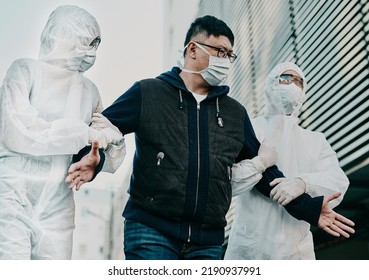 Man Breaking Covid Regulation Getting Taken Away Or Arrested By Healthcare Workers Wearing Hazmat Protective Suits. Male Removed For Not Following The Rules Or Restrictions Of Coronavirus Pandemic.