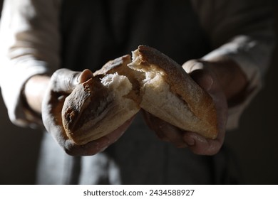 Man breaking loaf of fresh bread on dark background, closeup - Powered by Shutterstock