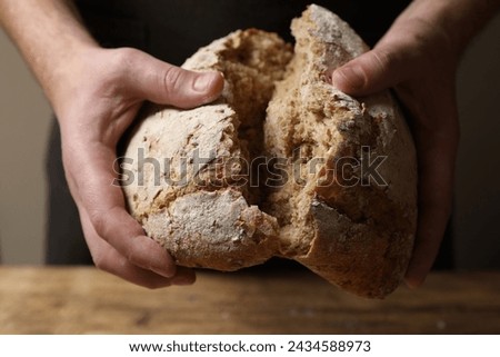 Man breaking loaf of fresh bread at wooden table, closeup