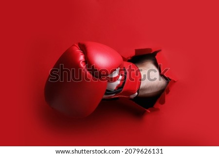Man breaking through red paper with boxing glove, closeup