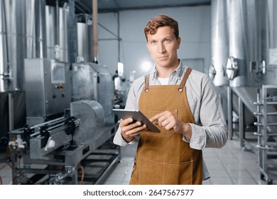 Man brewer using tablet in modern brewery with industrial equipment, control beer, food industry.