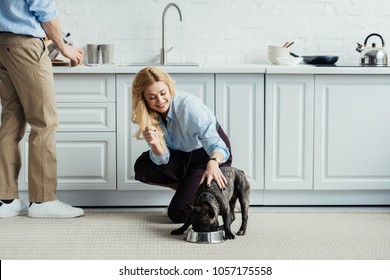 Man brewing coffee and blonde woman stroking french bulldog on kitchen floor - Powered by Shutterstock