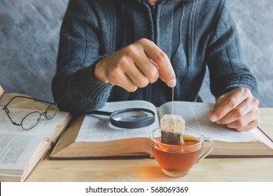 A Man Brewing Tea Bag With Glass Of Tea On Table During Reading Time