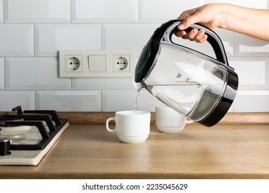 A man brews tea using boiling water from an electric kettle in the kitchen at home.Kettle for boiling water and making tea and coffee.Home appliances for hot drinks.Side view, space for text. - Powered by Shutterstock