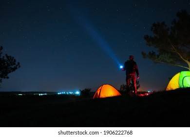 Man With Bright Flashlight Near Camping Tents Outdoors At Night