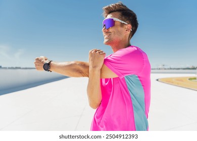 A man in a bright pink athletic shirt stretching his arms while smiling, preparing for a workout under a clear, sunny sky.

 - Powered by Shutterstock