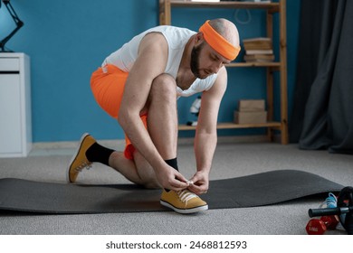 A man in bright sportswear is tying his sneakers, getting ready for a workout on a yoga mat at home - Powered by Shutterstock