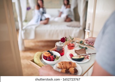 man bringing breakfast in bed for two female. lesbian, bisexual, threesome concept
