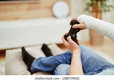 Man With Broken Arm In Plaster Cast Holding Controller And Playing In Videogame In Front Of TV. Game Addiction Concept