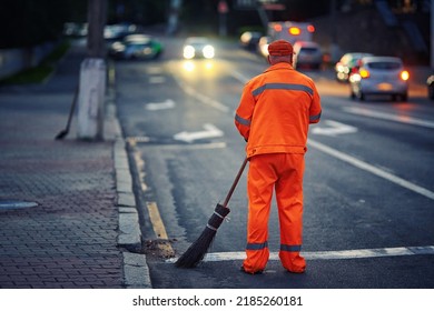 Man With Broom Clean City Road And Roadside At Night. Worker Cleans Roads, Streets, Footpaths With Broom, Night Work. Janitor Cleanup City From Garbage. Municipal Worker In Uniform Sweeping Street