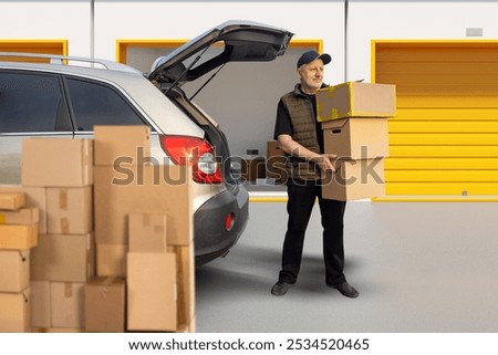 Man brought boxes to storage unit. Loader unloads car while standing near warehouse. Guy picks up parcels from pantry. Man near storage rooms with orange gates. Renting outdoor storage unit.