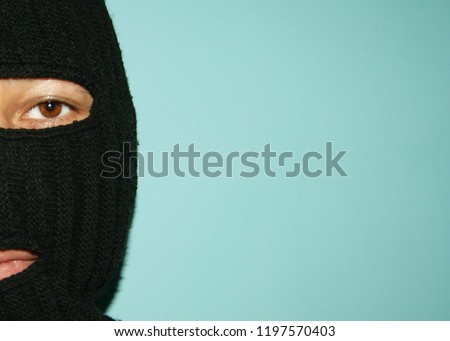 A man with brown eyes in a balaclava on a blue background.