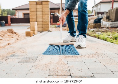 A man with a brush sweeps the paving slabs on the path near the house - general cleaning of the personal plot - Powered by Shutterstock