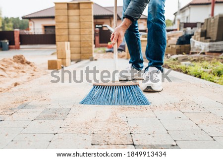 A man with a brush sweeps the paving slabs on the path near the house - general cleaning of the personal plot
