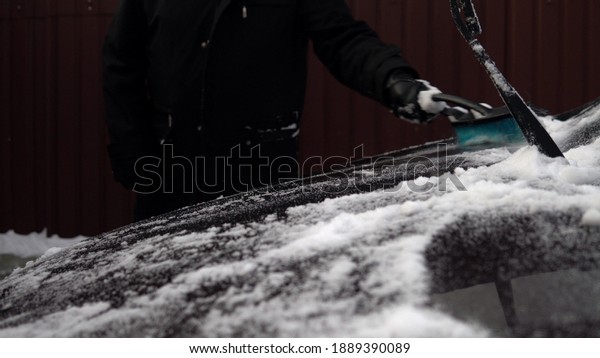 A man brushes off snow from the\
hood of a car. Winter in Russia, the car was covered with\
snow