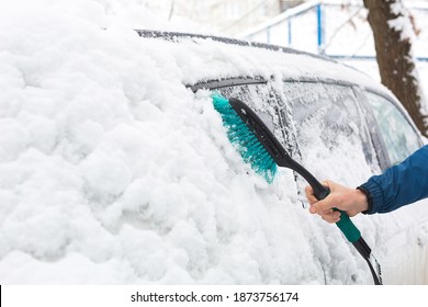 A man brushes snow from a car after a snowfall. A hand in a blue jacket with a car broom on the white body. Winter weather conditions - Powered by Shutterstock