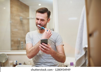 Man Brushing His Teeth And Using Mobile Phone 