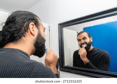 Man brushing teeth with focused expression in bathroom mirror