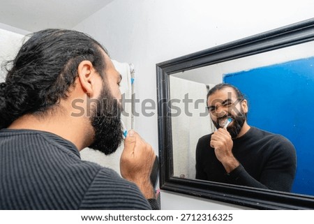 Man brushing teeth with focused expression in bathroom mirror