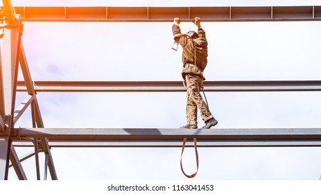 A man builder in a construction uniform without insurance moves around the construction of mettalical structures high above the ground. Violation of safety at the construction site