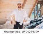 Man builder. Contractor for construction company. Architect in unfinished building. Builder in wooden modular house under construction. Male engineer holding a model of a miniature wooden house