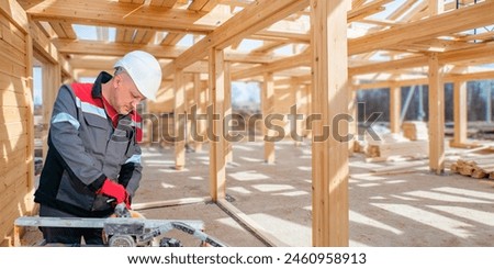 Man builder. Engineer works at construction site. Builder in gray uniform. Foreman inside unfinished house. Contractor uses equipment for construction. Frame of wooden house above man builder
