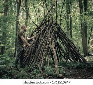 Man building a  survival  shelter in the forest. Shelter in the woods from tree branches. - Shutterstock ID 1761513947