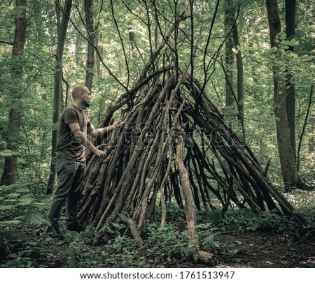 Man building a  survival  shelter in the forest. Shelter in the woods from tree branches.