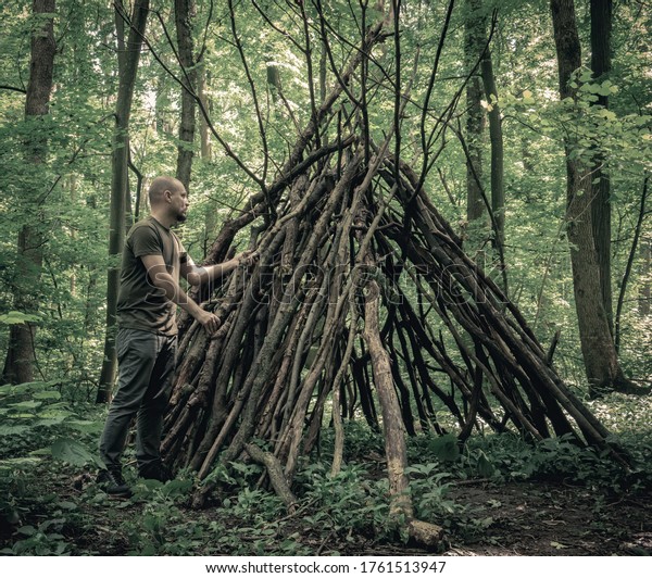 Man building a  survival  shelter in\
the forest. Shelter in the woods from tree\
branches.
