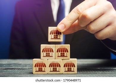 A man builds a pyramid from blocks of business shops. Building a successful business empire. Expansion and competitive growth. Franchise concession concept. Commercial network development.