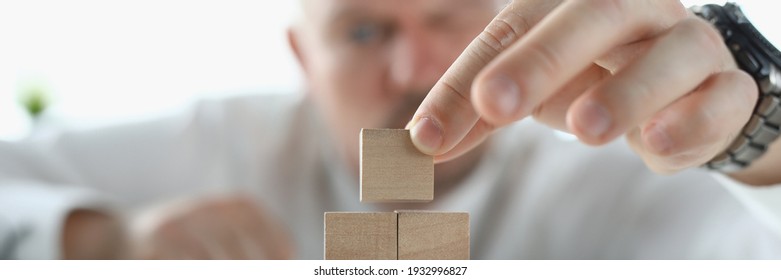 Man builds pyramid from wooden cubes in office. Small and medium business development concept - Shutterstock ID 1932996827