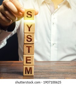 The man builds a tower of blocks the word System. Creation of a system, organization of processes, systematization. Establishment of a new order. Regulation work. Stability and invulnerability - Shutterstock ID 1907100625