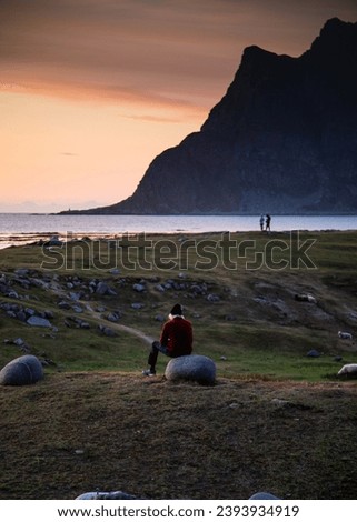 Similar – Man sitting on a cliff of a fjord with low sun on the European Arctic Ocean