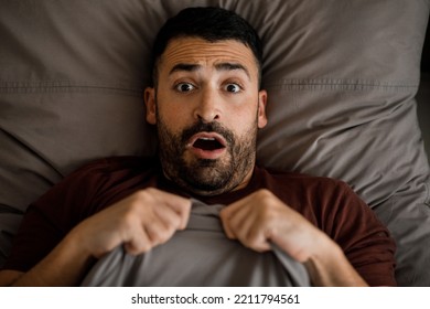 A man in a burgundy T-shirt is scared in bed looking at the camera