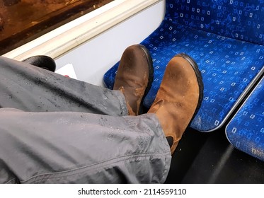 Man Bus Passenger In Wet Dirty Boots Puts His Muddy Feet On Seat Opposite. The Seats Already Are Stained With Mud Because It Is Raining And Slushy Outside. Bad Behavior Example In A Public Area