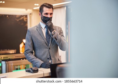 Man In A Business Attire Standing At A Desk While Taking Off A Dark Mask From His Mouth