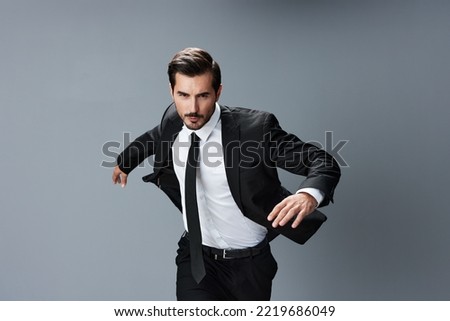 Man business happy in jacket and shirt jumping and running on gray background raised hands up serious face. Successful business