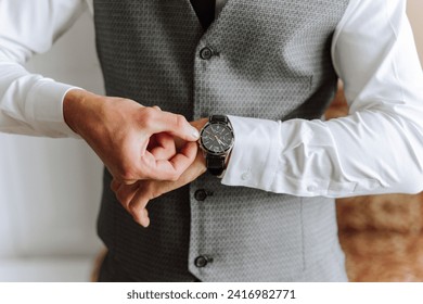 A man in a business suit is adjusting his wristwatch, a mug of coffee is on the table in his room. Close-up photo of a wristwatch.