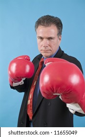 A man in a business suit with boxing gloves on, ready to punch the camera.