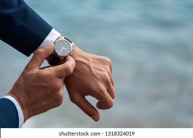 A Man In A Business Suit Checking A Wrist Watch On His Hand On Background  Sea