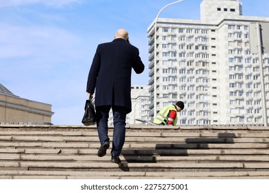 Man in a business suit and coat with leather briefcase in hand climbing stone stairs in city and talking by mobile phone. Concept of career, success, moving to the top, official or businessman - Powered by Shutterstock